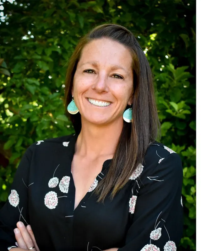 Dr. Ricki Walker smiling outdoors in front of green trees
